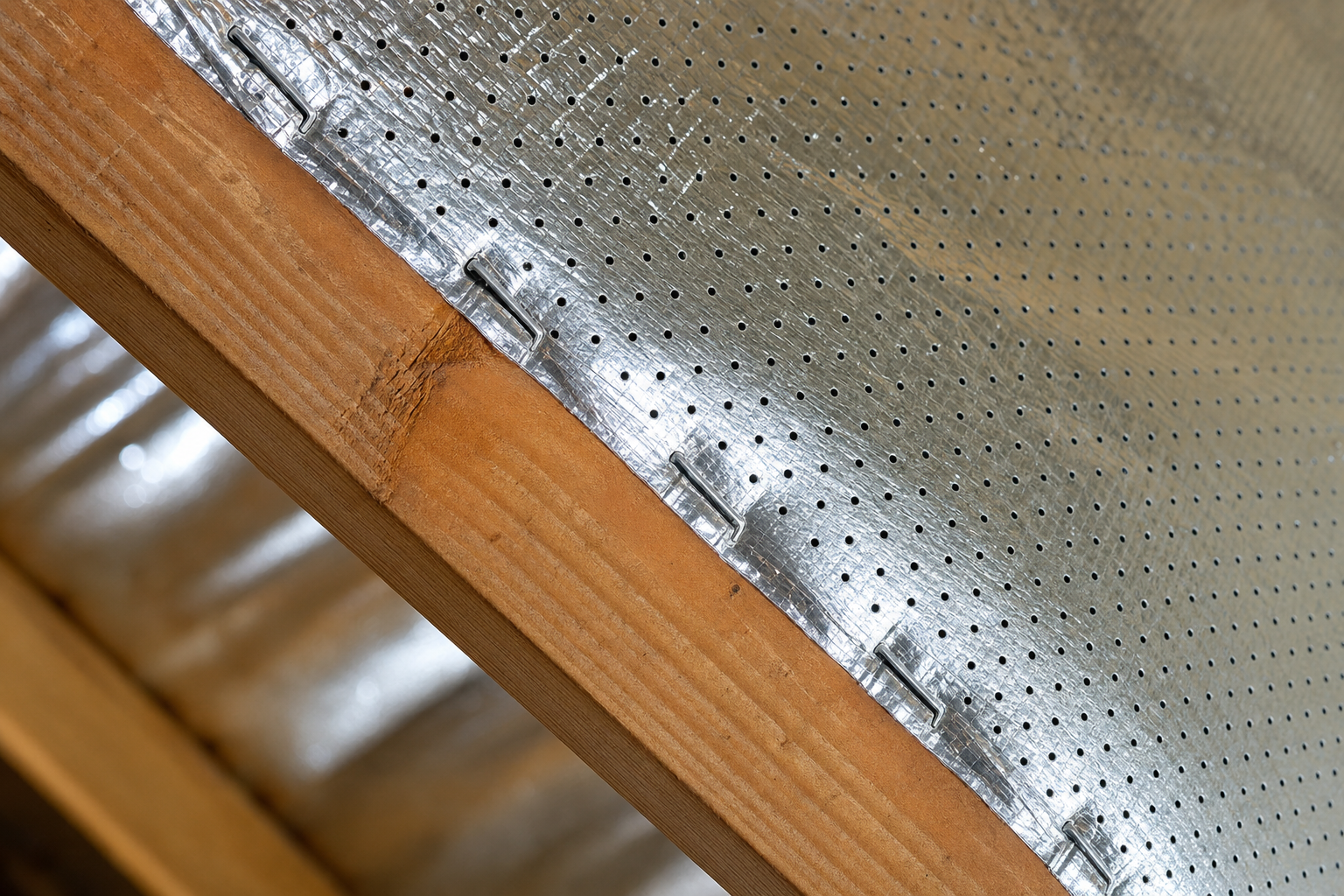 Close-up of perforated double-sided aluminum radiant barrier foil stapled to a Houston attic rafter — DC Pines