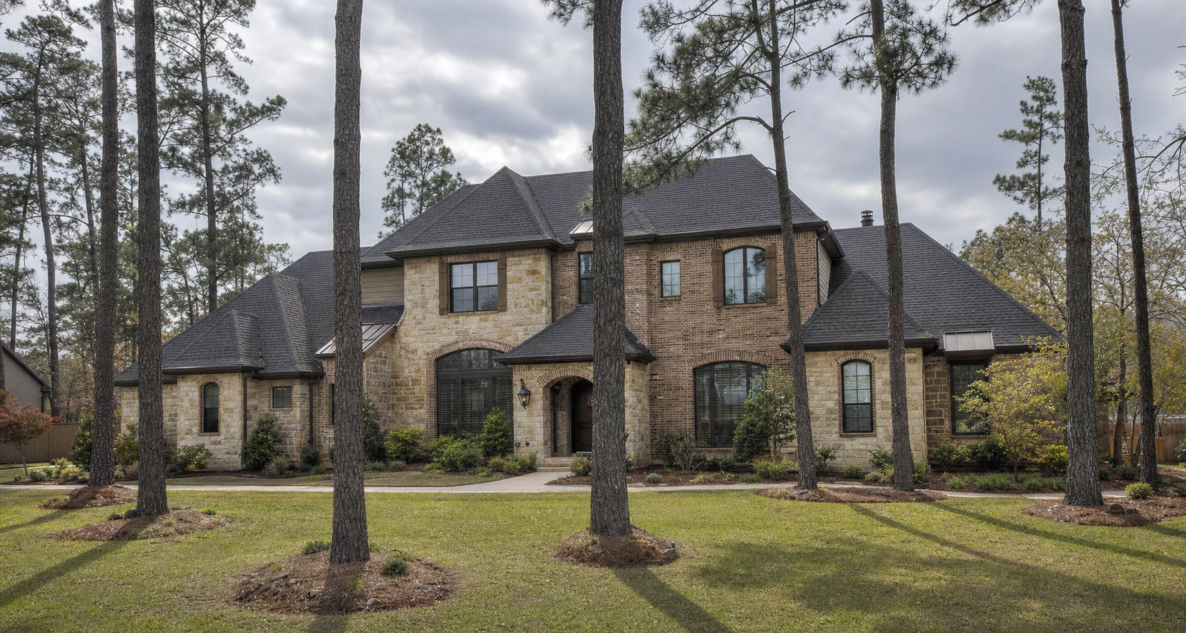 Stone-and-brick Woodlands Texas home with a muted charcoal architectural shingle roof under tall pines