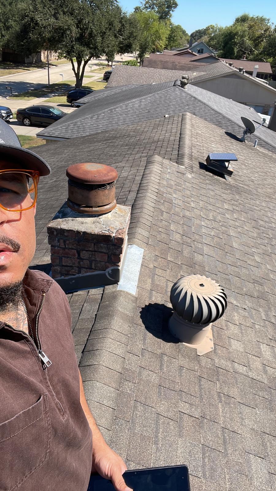 DC Pines Roofing technician on a Houston rooftop checking a turbine vent and chimney flashing during service