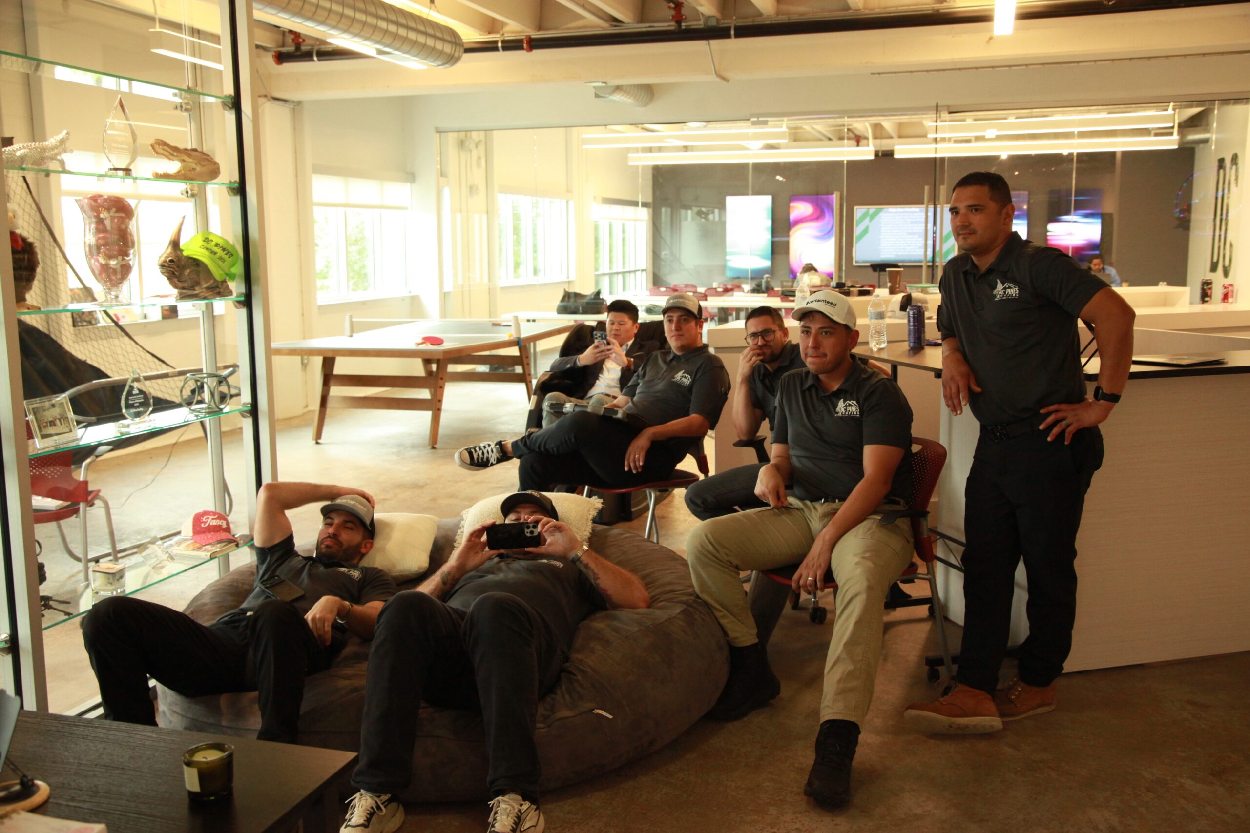 DC Pines Roofing team members gathered at Houston headquarters lounge with company trophies