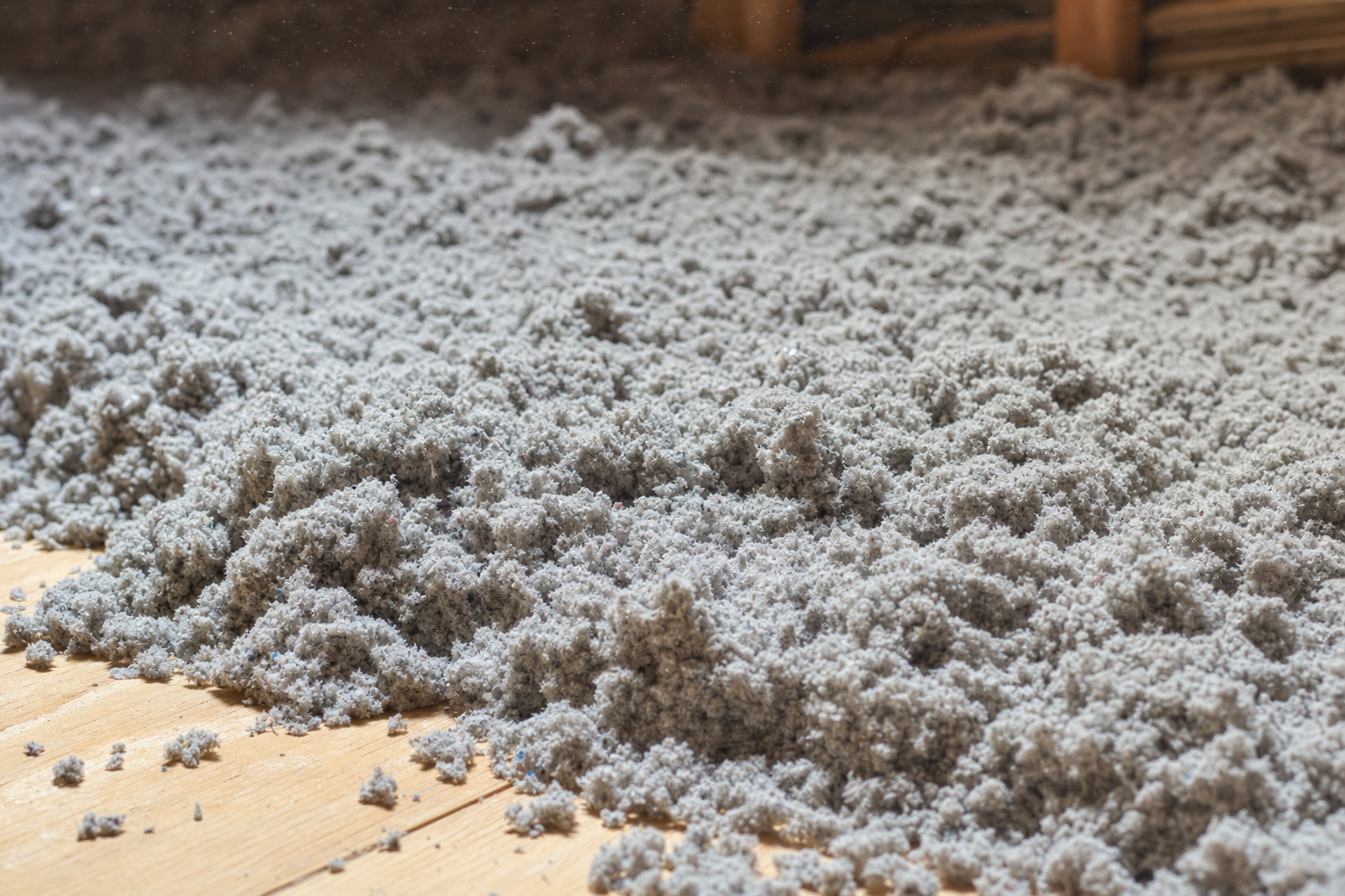 Close-up of gray blown-in cellulose attic insulation showing loose fibrous texture on plywood decking