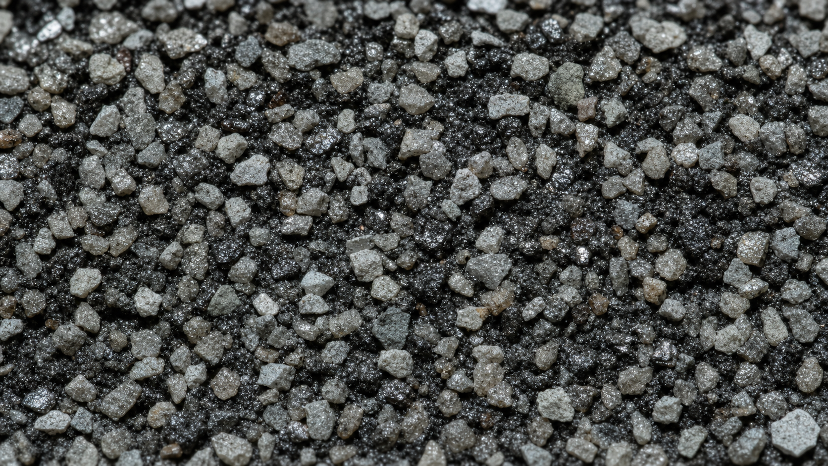 Macro of a light gray asphalt shingle surface showing the ceramic granules with reflective silver flecks embedded in the asphalt
