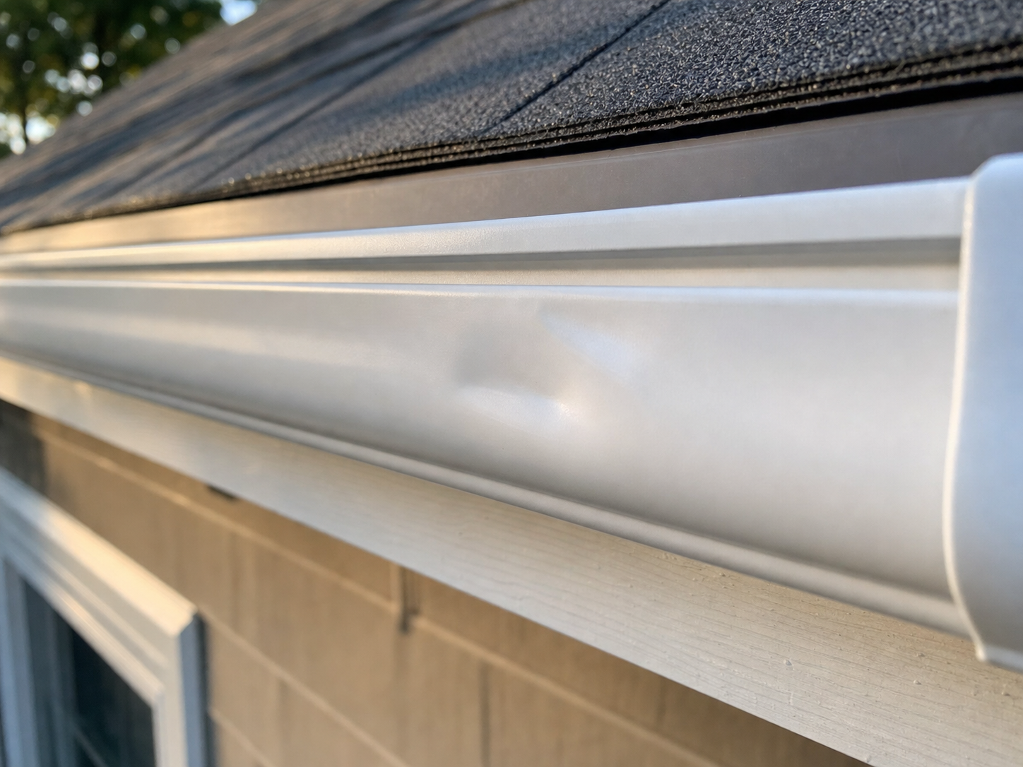 Detail of a slightly dented aluminum gutter front face caused by a ladder rung leaning against it