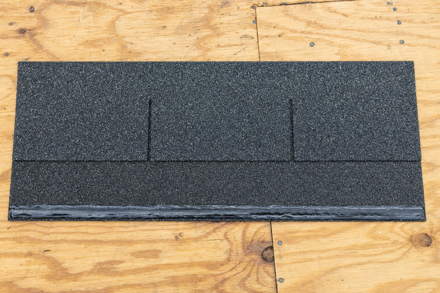 Single manufacturer-made asphalt starter strip shingle on roof deck showing the continuous factory-applied self-adhering sealant bead along its leading edge