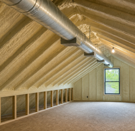 Interior of a Houston residential conditioned unvented attic with tan spray foam on the underside of the roof deck and exposed HVAC duct trunk