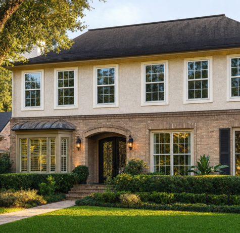 Two-story Houston brick and stucco home elevation with white double-hung windows across the facade in late afternoon sun