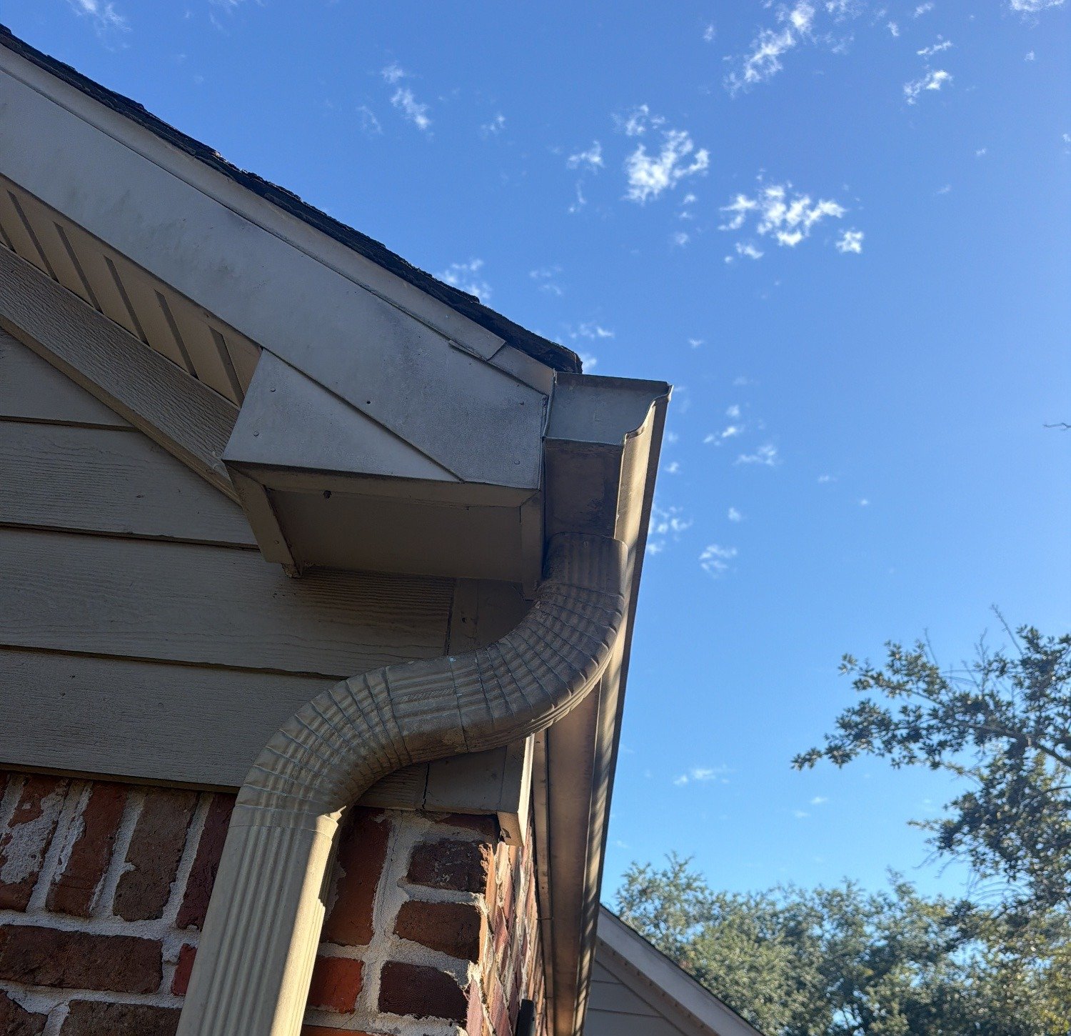 Gutter end and downspout outlet at a roof corner on a brick and siding Houston home