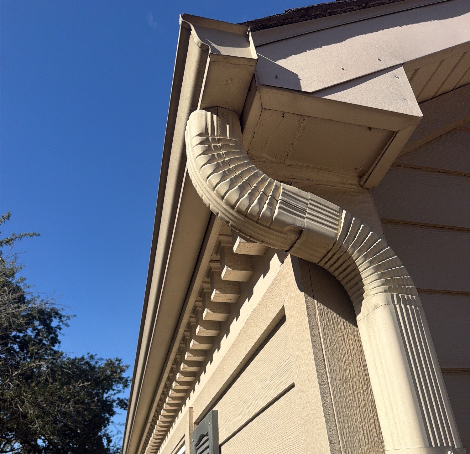 Downspout elbow at the outlet of a seamless aluminum gutter on a Houston home