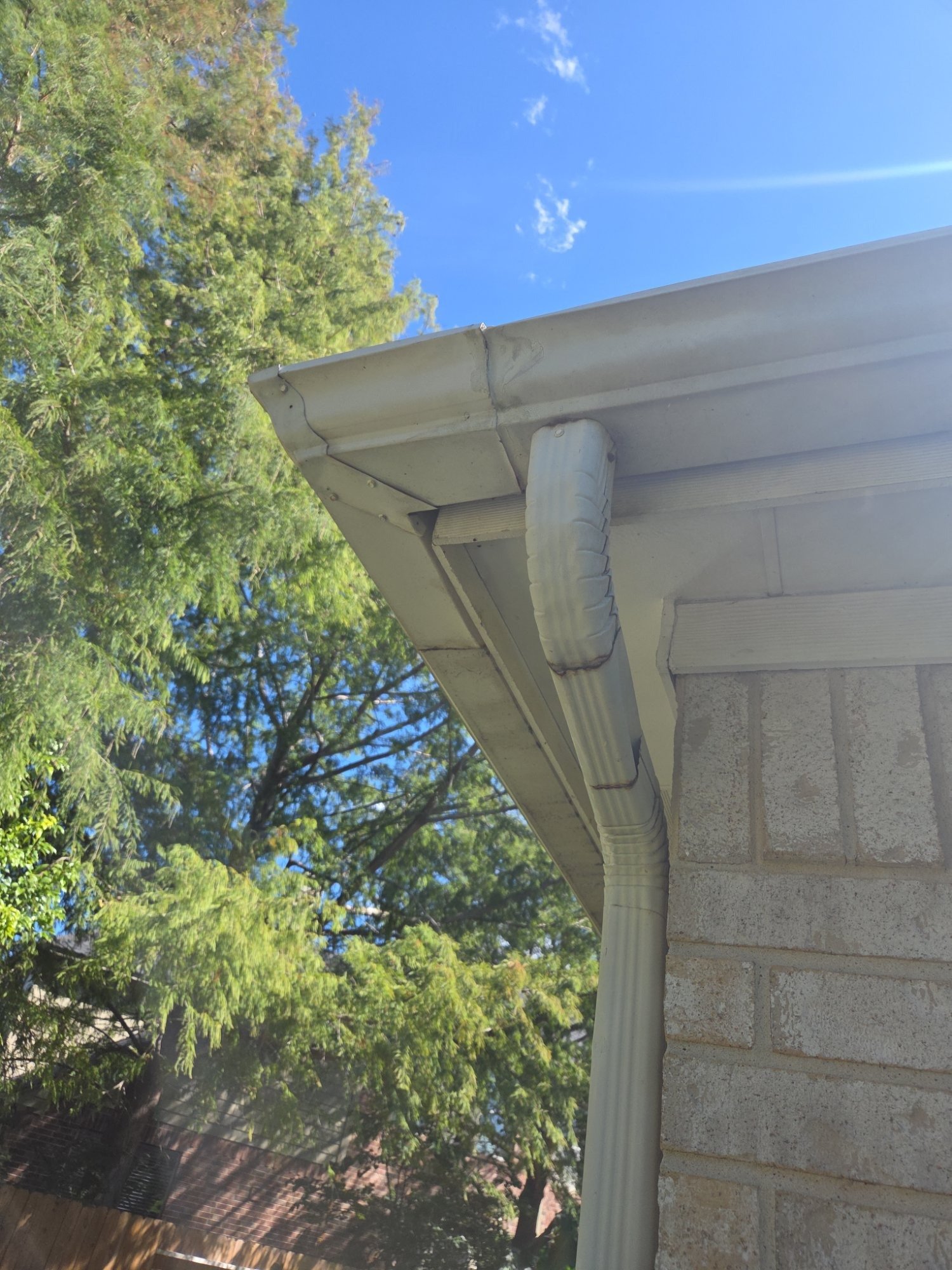 Gutter corner and downspout on a brick Houston home under tall trees on a clear fall day