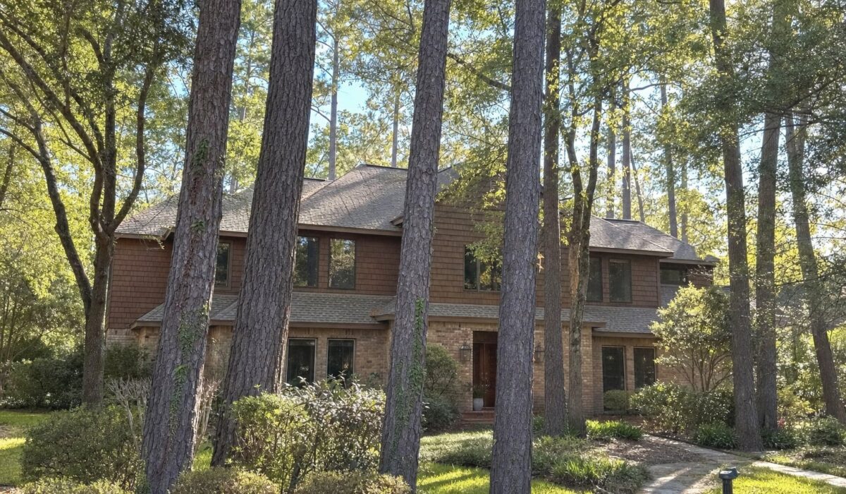 Two-story home in The Woodlands surrounded by tall loblolly pine trees, showing the pine canopy over the roof and gutter line